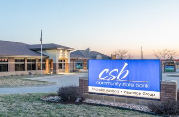 A bank sign partially buried in grass, indicating the location of the bank branch nearby.