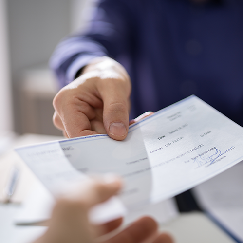 Close-up of a hand handing over a receipt to another person, potentially a customer, in a blurred office setting.