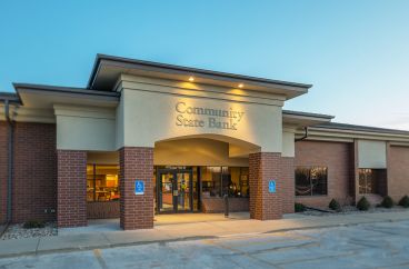 Modern building entrance with a welcoming facade, featuring large windows, warm lighting, and brick exterior under a clear sky.