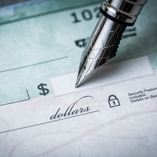 Close-up of a fountain pen writing on a personal check, focusing on the dollar sign and signature line.