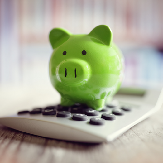 A bright green piggy bank sits atop a white calculator, suggesting savings or financial planning.