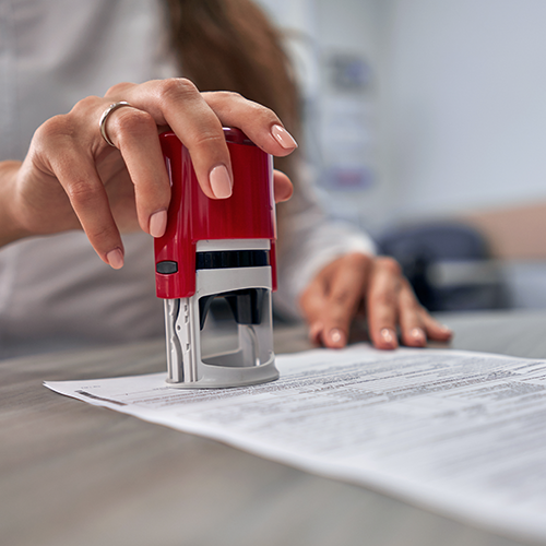 A person using a red stamp to mark a document on a desk, focused and in an office setting.
